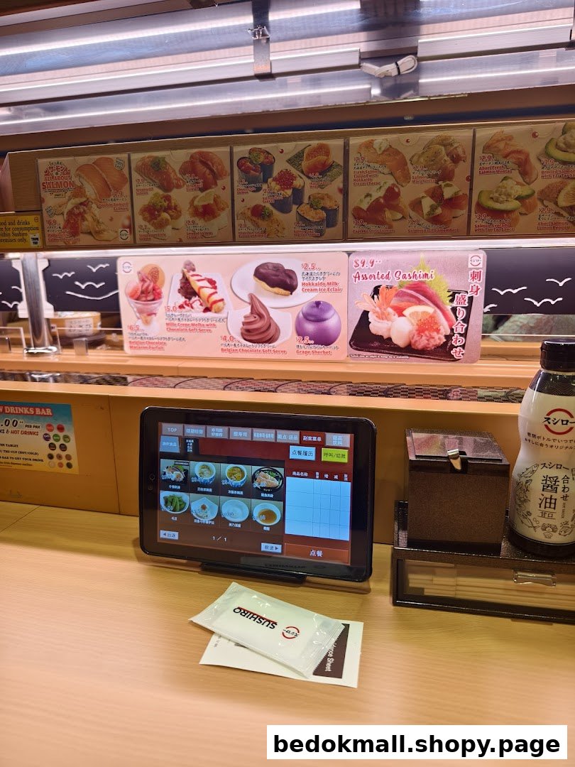 Sushi restaurant interior showing conveyor belt, ordering tablet, and food displays.