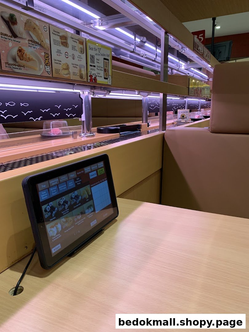Interior view of a sushi restaurant with a conveyor belt and ordering tablet.