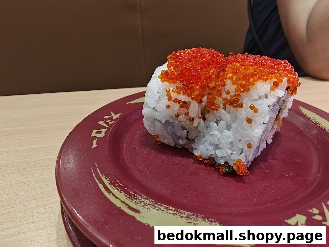 Close-up of a sushi roll topped with roe on a red plate.