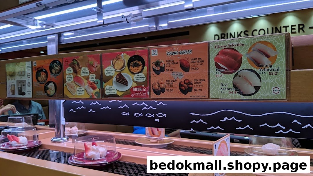 Sushi conveyor belt restaurant with overhead menus displaying various food items and prices.