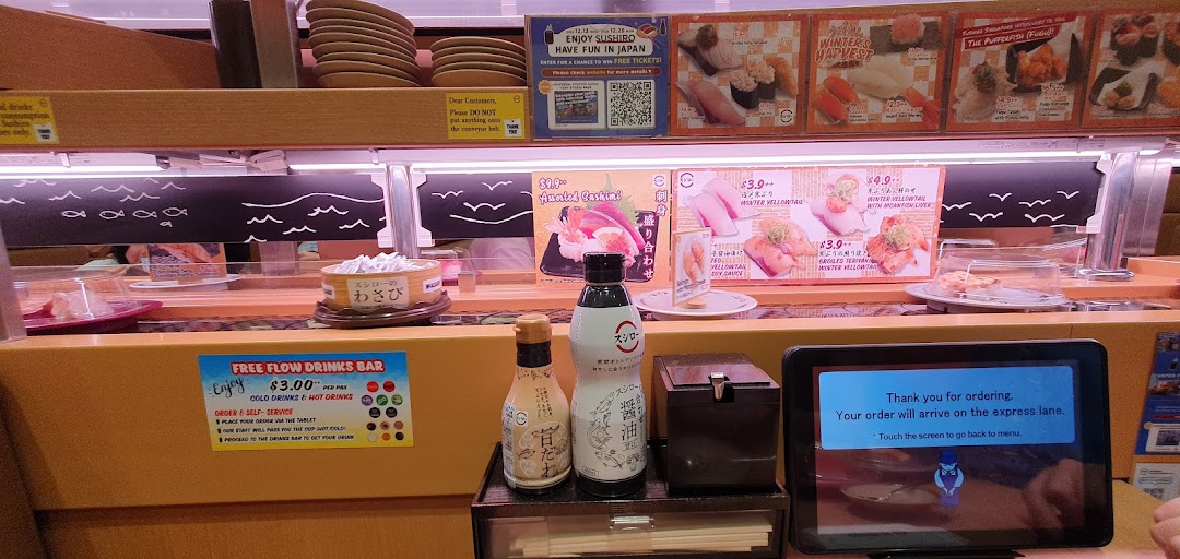 Interior view of a sushi restaurant with conveyor belt, ordering tablet, and condiments.