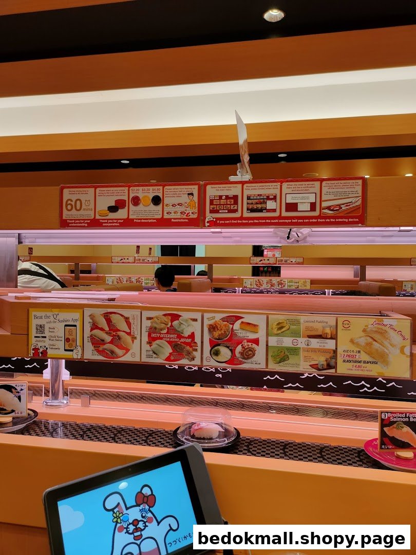 Sushi restaurant interior showing conveyor belt, ordering tablet, and overhead signs.