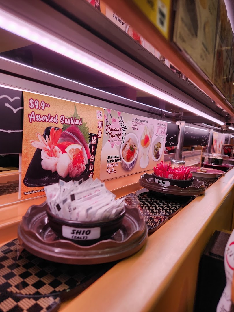 Interior view of a sushi restaurant with a conveyor belt and promotional posters.