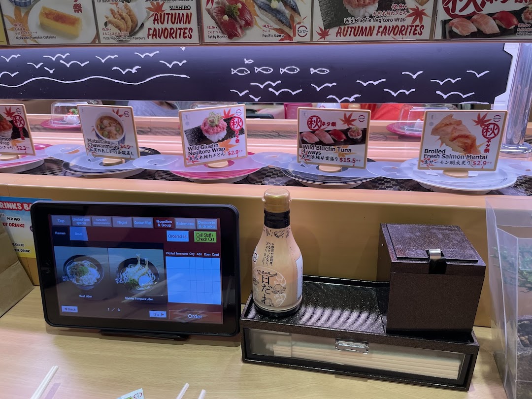 Sushi restaurant interior with conveyor belt, ordering tablet, and food items.