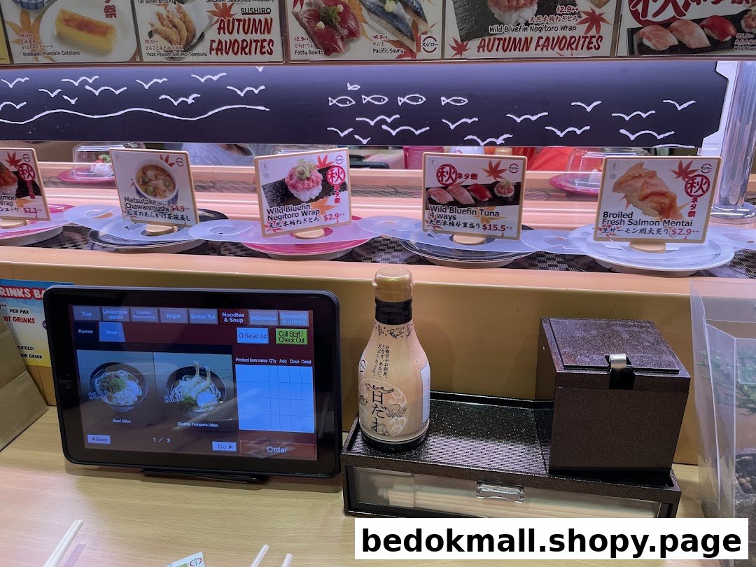 Sushi restaurant interior with conveyor belt, ordering tablet, and food items.