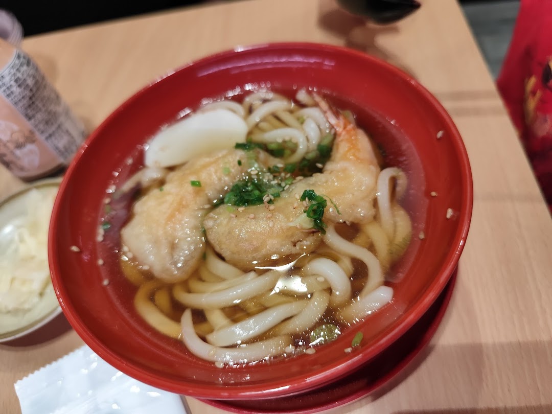 A red bowl of udon noodles with tempura in broth on a wooden table.
