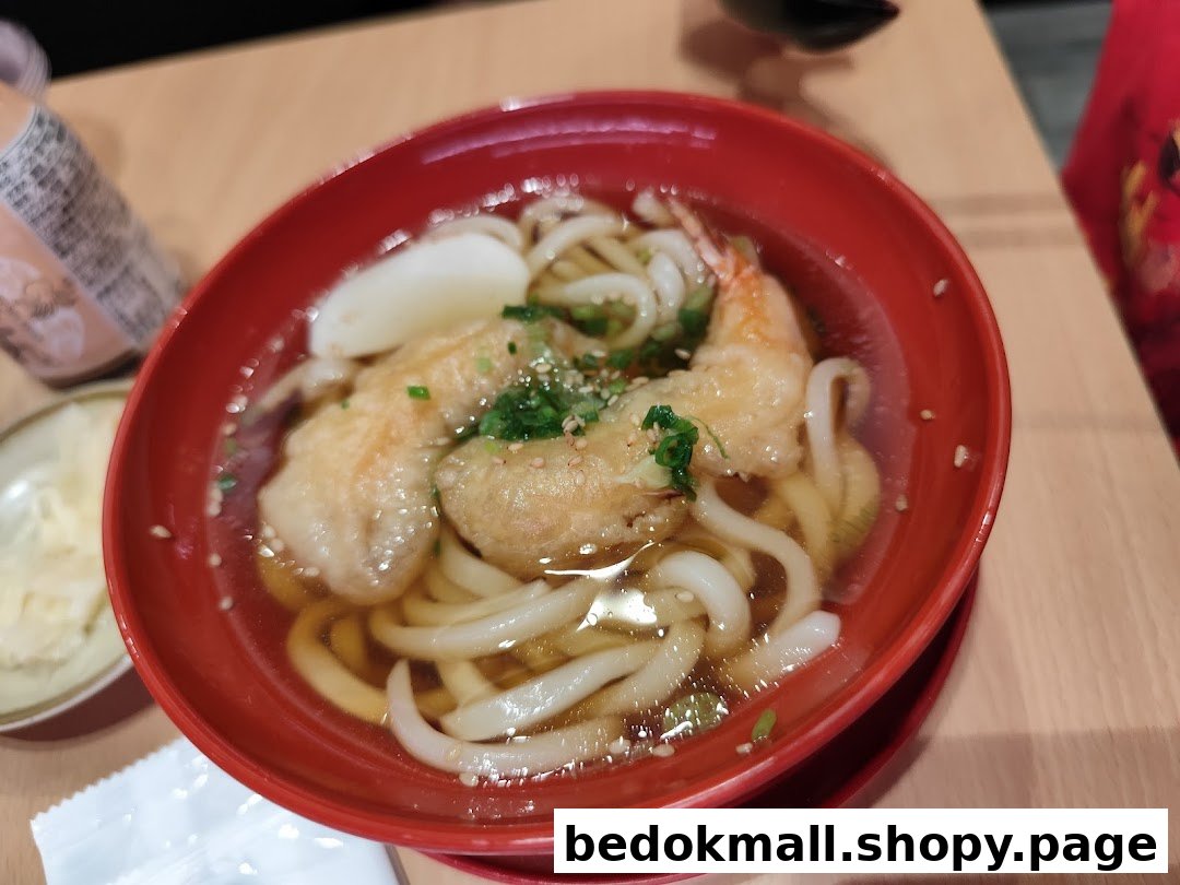 A red bowl of udon noodles with tempura in broth on a wooden table.