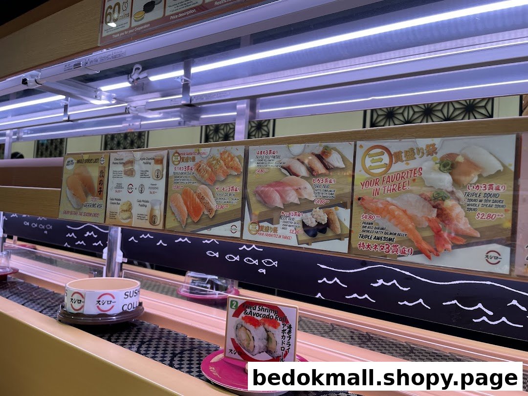 Sushi restaurant interior with conveyor belt and overhead menu displays showing various dishes.