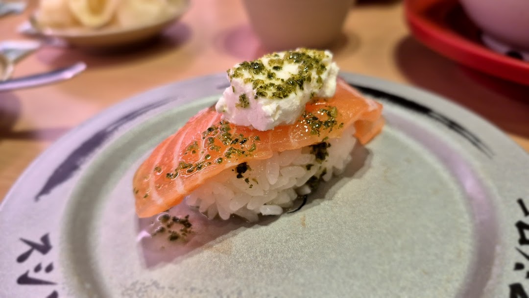 Close-up of salmon sushi with cream cheese and green seasoning on a plate.
