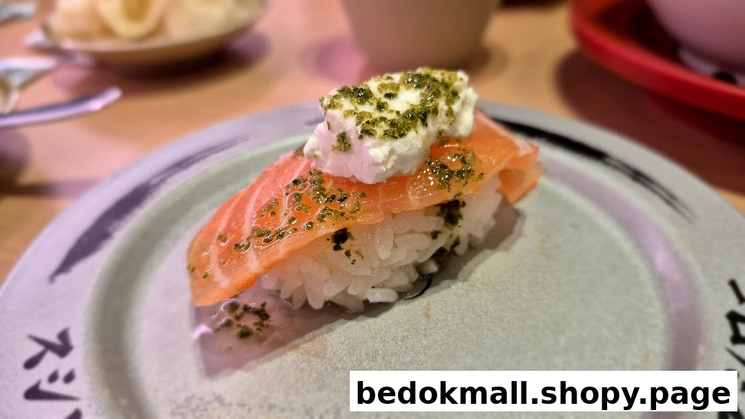 Close-up of salmon sushi with cream cheese and green seasoning on a plate.