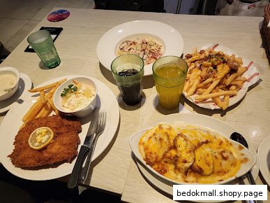 Table laden with various dishes including fried cutlet, fries, pasta, and baked items.