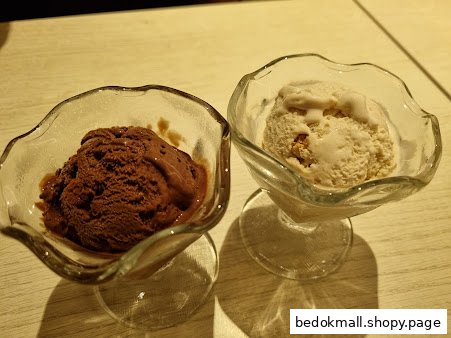 Two scoops of ice cream in glass bowls on a light-colored table.