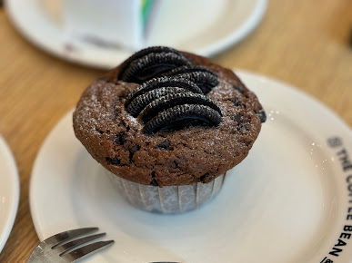 A chocolate muffin topped with Oreo cookies and powdered sugar on a white plate.