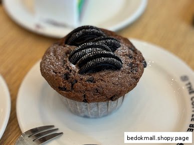 A chocolate muffin topped with Oreo cookies and powdered sugar on a white plate.