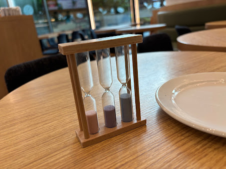 An hourglass and a white plate on a wooden table inside a cafe.