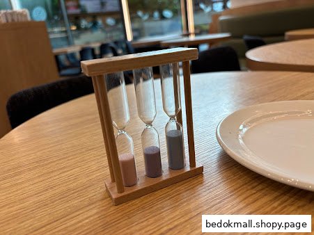 An hourglass and a white plate on a wooden table inside a cafe.