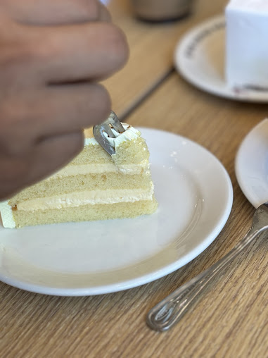 A hand uses a fork to eat a slice of cake on a white plate.
