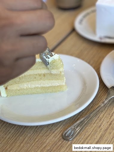 A hand uses a fork to eat a slice of cake on a white plate.