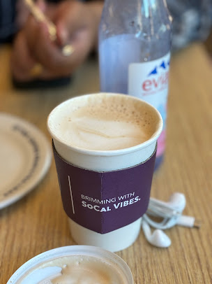 Coffee cup with sleeve, Evian bottle, and earbuds on a table.