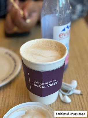 Coffee cup with sleeve, Evian bottle, and earbuds on a table.