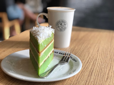 A slice of green cake and a coffee cup on a wooden table.