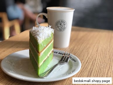 A slice of green cake and a coffee cup on a wooden table.