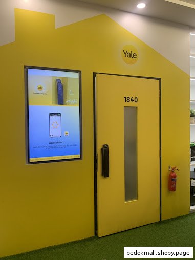 Yellow house-shaped display with a door and digital screen showcasing Yale smart home products.