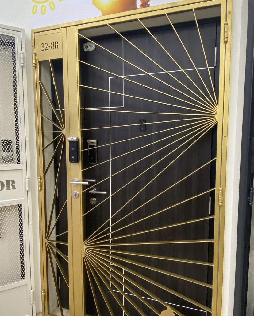 A golden security gate with a sunburst design in front of a dark door.