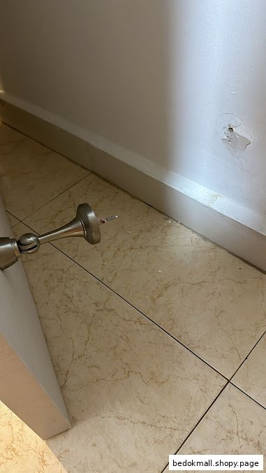 A door stopper, tiled floor, and damaged wall with a hole.