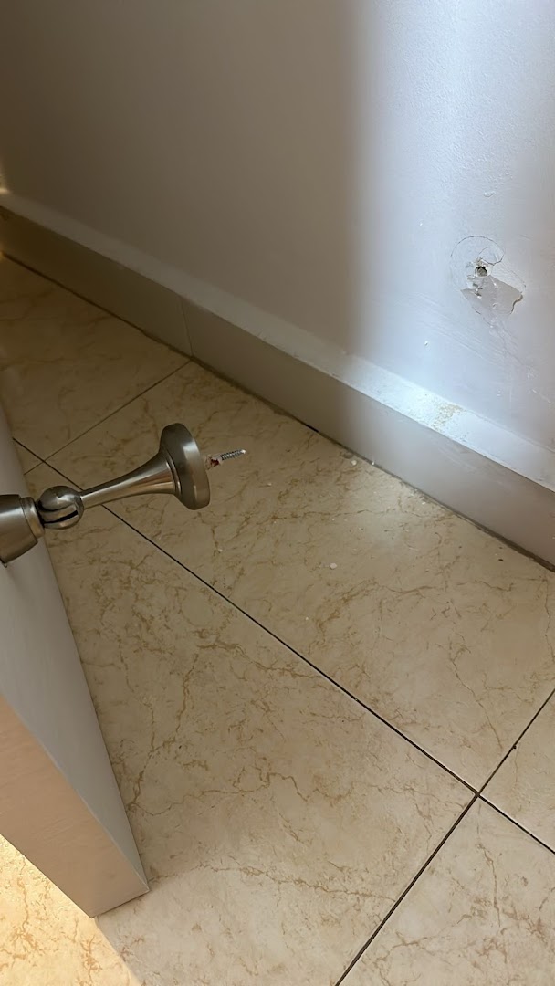 Metallic door stopper on tiled floor with damaged wall.