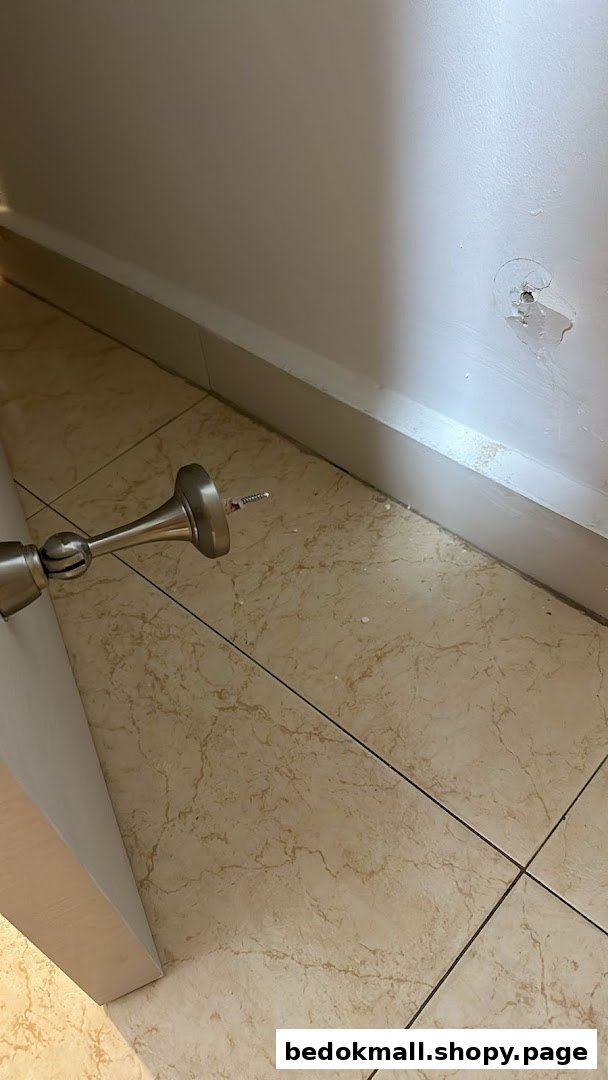 Metallic door stopper on tiled floor with damaged wall.