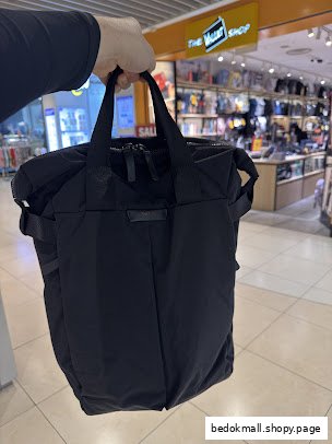 Person holds a black bag inside The Wallet Shop, displaying products.