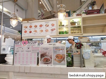Interior view of a cafe counter with staff, menu board, and promotional displays.