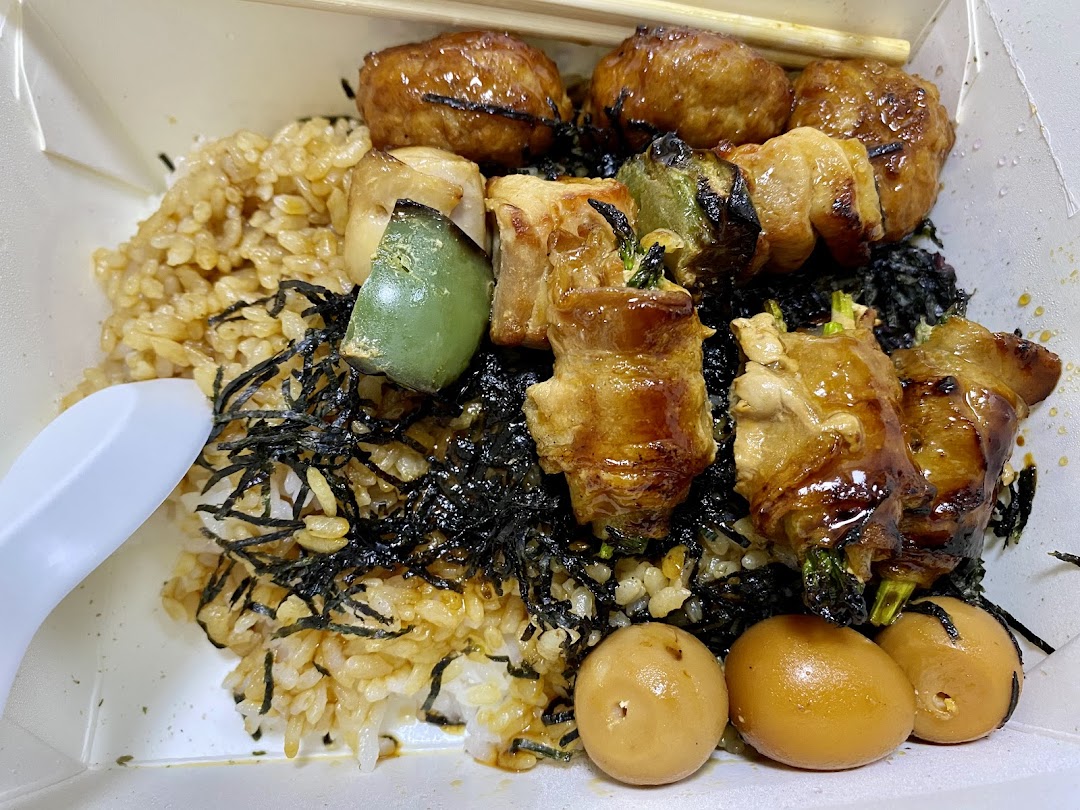 Close-up of a meal with rice, skewers, and eggs in a takeout box.
