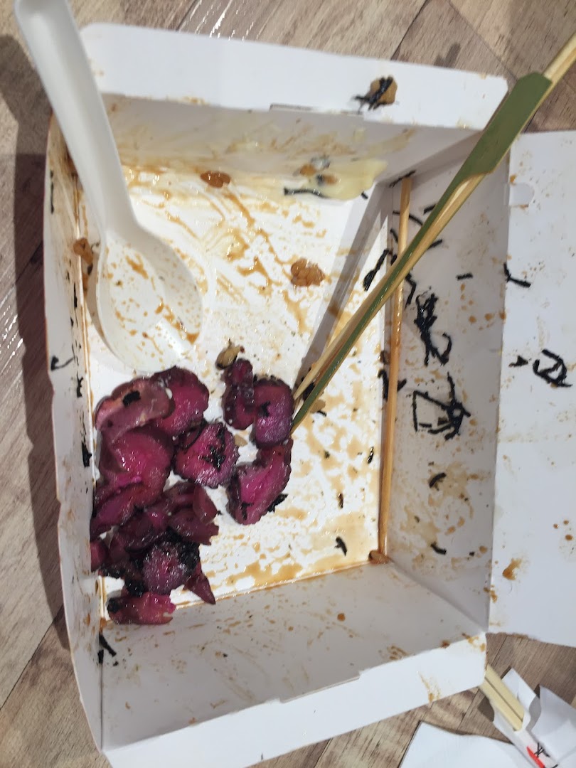 An open, stained takeaway box with food remnants, a spoon, and a skewer.