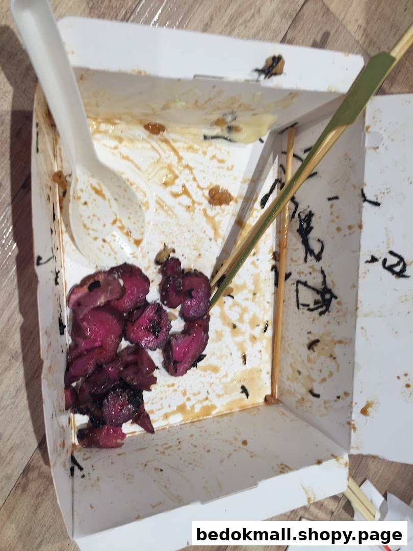 An open, stained takeaway box with food remnants, a spoon, and a skewer.