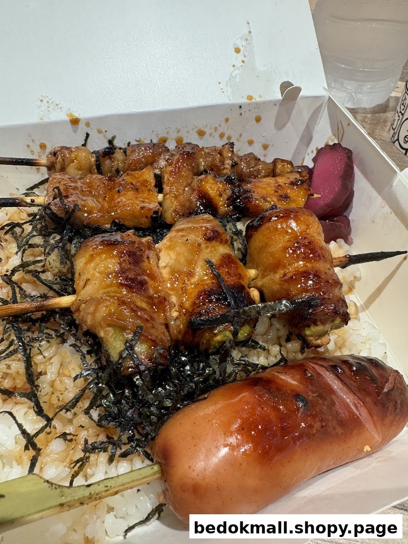 A takeaway box filled with grilled skewers, rice, and a sausage.