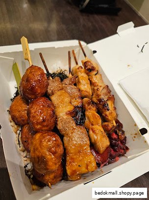 A box of grilled skewers and meatballs served over rice.