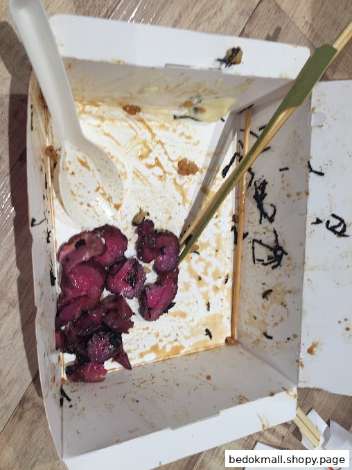 Leftover food in a takeout box with a spoon and skewer.
