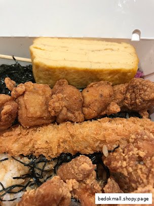 Close-up of a bento box with fried chicken, shrimp, tamagoyaki, and rice.