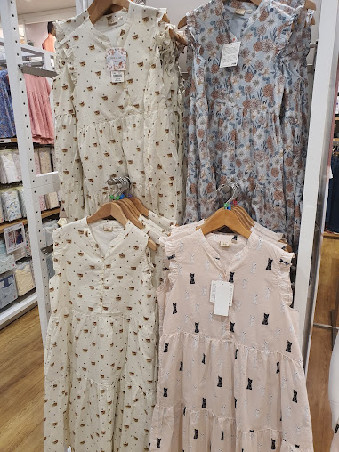 Four patterned dresses, including cat and floral designs, hanging on display racks.