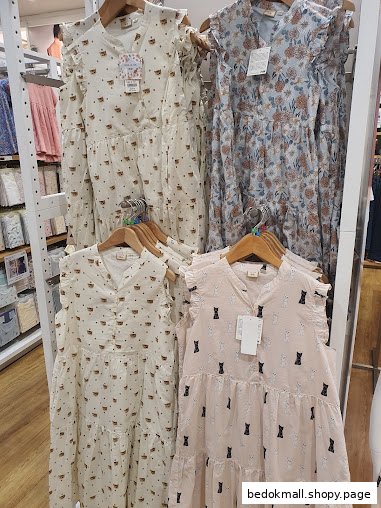 Four patterned dresses, including cat and floral designs, hanging on display racks.