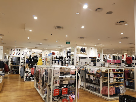 Interior view of a brightly lit clothing store with various apparel displays and mannequins.