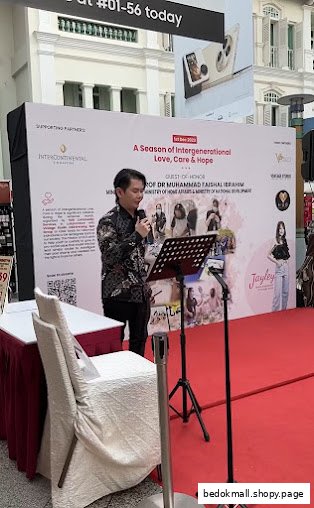 Man speaking at an event with a large banner and red carpet.