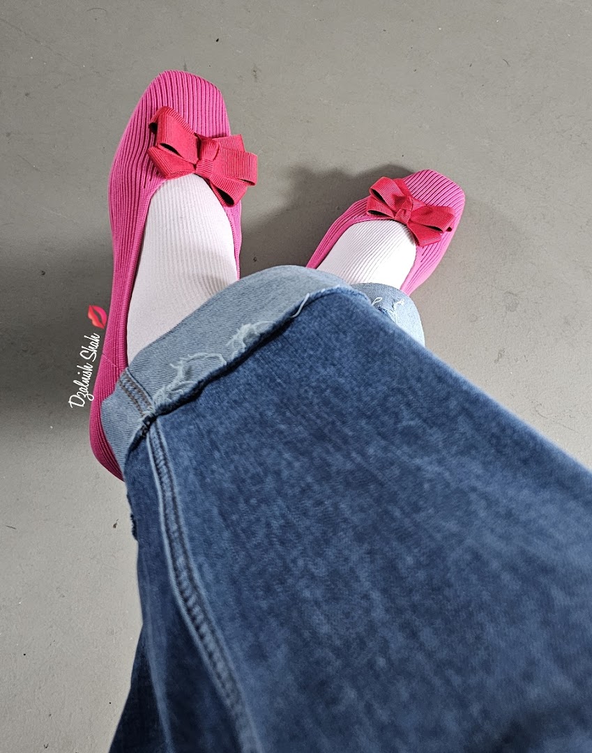 Person wearing pink shoes with bows, white socks, and blue jeans.
