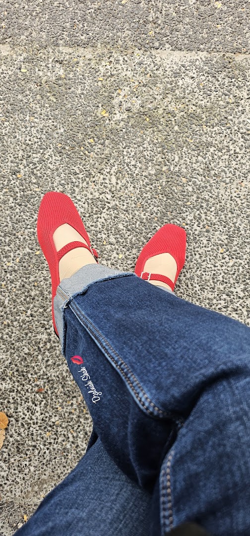 Person wearing blue jeans and red shoes on a textured ground.