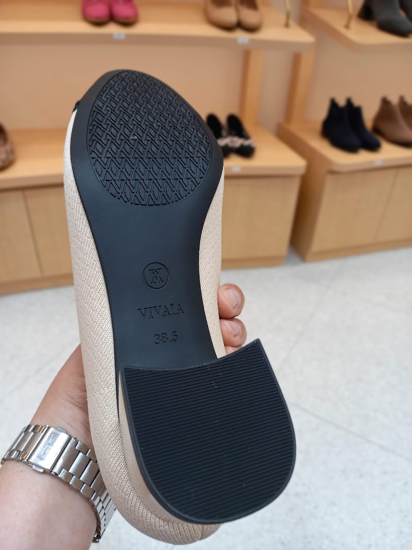 A hand holds a shoe, showing its sole, inside a shoe store.