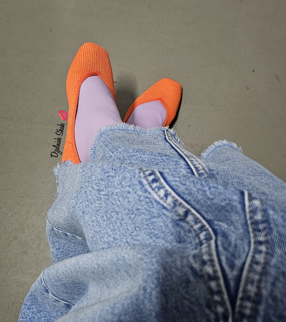 Person wearing orange shoes and purple socks with blue denim pants.