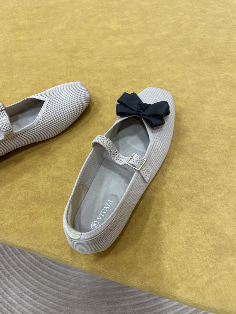 A pair of beige shoes with a black bow on a yellow surface.