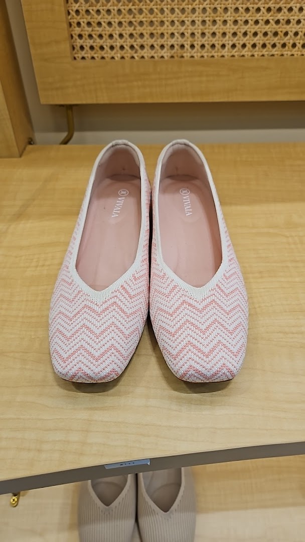 A pair of pink and white patterned flat shoes displayed on a wooden shelf.